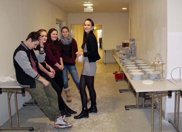 Eine Gruppe junger Leute steht in einem Flur mit gedeckten Tischen.