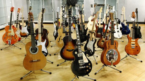Eine Sammlung verschiedener Gitarren steht auf Ständern in einem Raum.