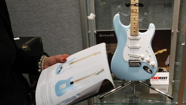 Eine hellblaue E-Gitarre steht in einer Vitrine, während eine Person einen Katalog betrachtet.