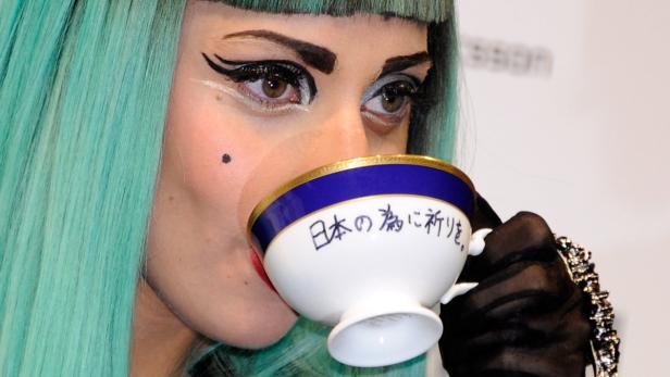 Eine Frau mit türkisfarbenem Haar trinkt aus einer Teetasse mit japanischer Schrift.