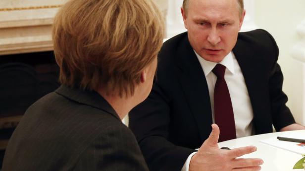 Wladimir Putin gestikuliert während eines Treffens mit einer Person, vermutlich Angela Merkel.