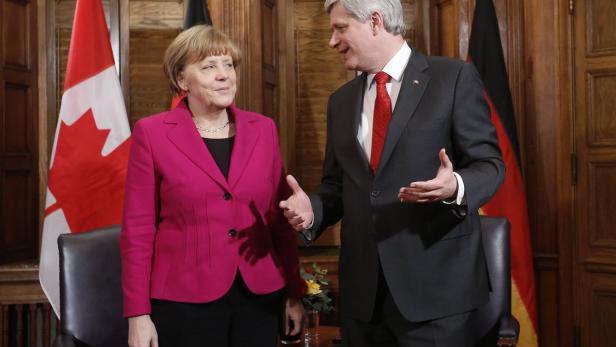 Angela Merkel und Stephen Harper stehen vor deutschen und kanadischen Flaggen.