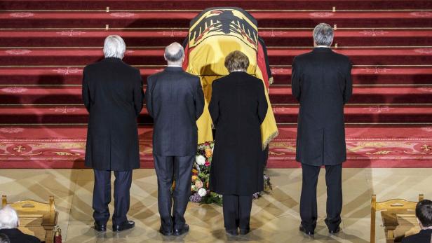 Trauergäste stehen vor einem mit der deutschen Flagge bedeckten Sarg.