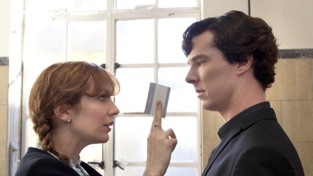 Eine Frau zeigt Benedict Cumberbatch eine Visitenkarte.