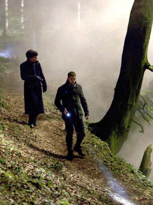 Zwei Männer mit Taschenlampen gehen einen nebligen Pfad im Wald entlang.