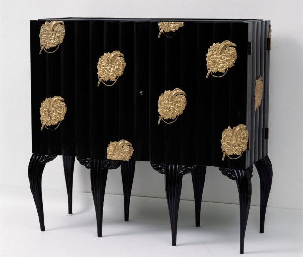 Ein schwarzer Schrank mit goldenen floralen Applikationen und filigranen Beinen.