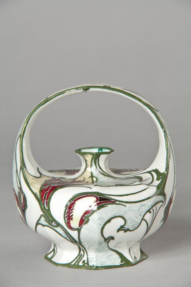 Eine verzierte, weiße Keramikvase mit Henkel und floralen Motiven in Rot und Grün.