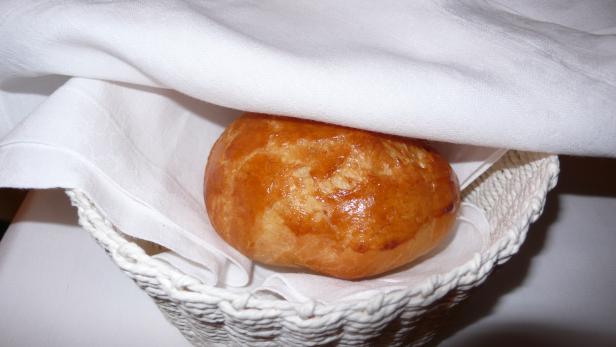 Ein Brötchen liegt in einem weißen Korb unter einer weißen Stoffserviette.