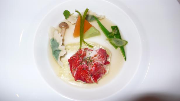 Ein Teller mit Hummer, Ravioli und Gemüse in einer hellen Brühe.