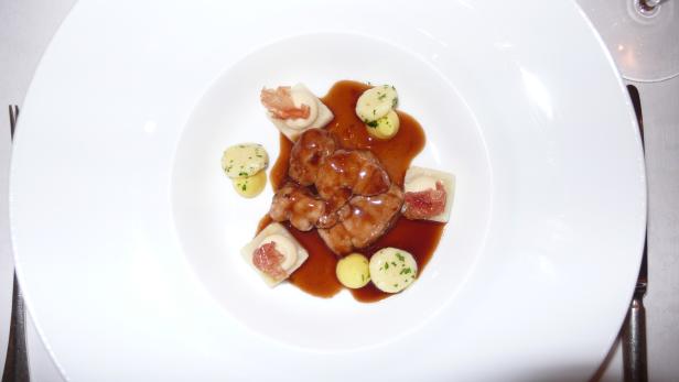 Ein Teller mit Fleisch, Ravioli und Kartoffeln in einer braunen Soße.