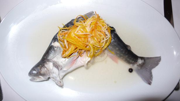 Ein ganzer, gekochter Fisch wird mit Julienne-Gemüse auf einem Teller serviert.