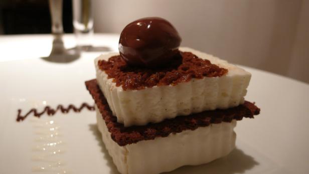 Ein Dessert mit einer Kugel Schokolade auf einer weißen Creme zwischen zwei Schokoladenböden.