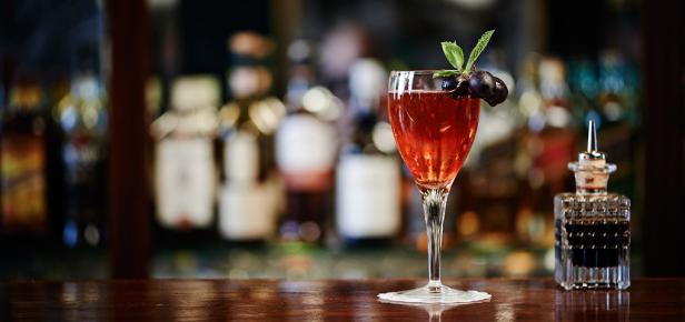 Ein Cocktail mit dunklen Trauben und Minze steht auf einer Bar.