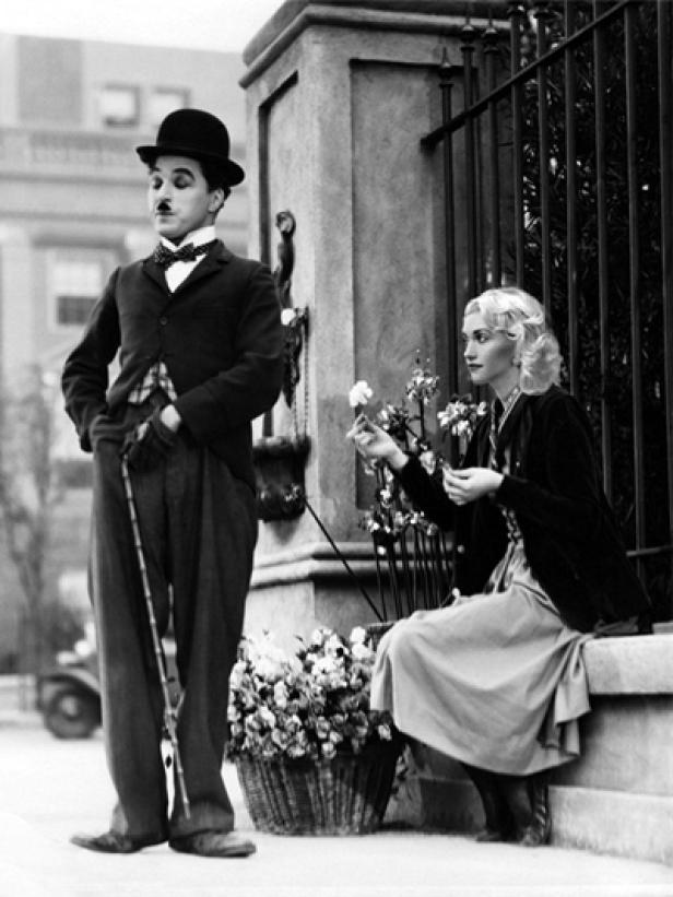 Charlie Chaplin steht neben einer Frau, die eine Blume hält.