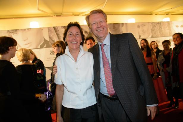 Eine Frau im weißen Hemd und ein Mann im Anzug posieren lächelnd für ein Foto.