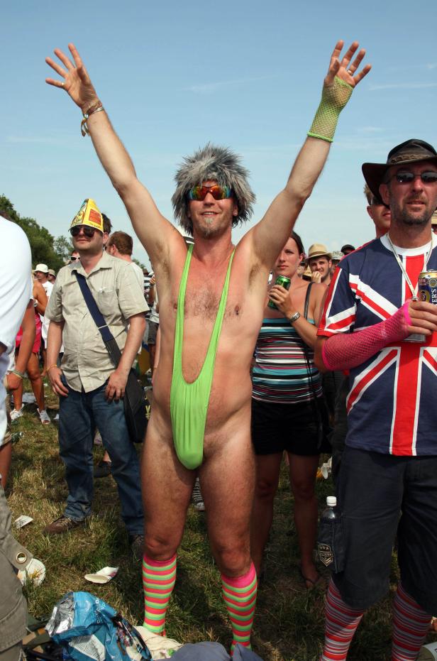 Ein Mann in einem grünen Mankini und gestreiften Socken steht auf einem Festivalgelände.