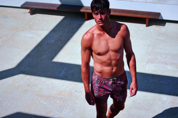 Ein Mann mit Badehose steht auf einer Terrasse.