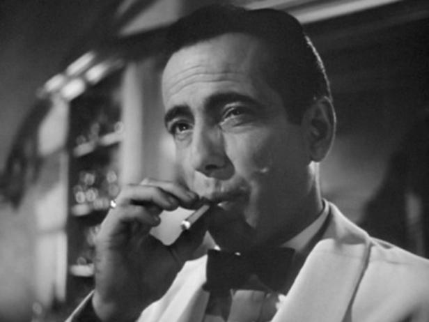 Schwarzweißporträt von Humphrey Bogart, der eine Zigarette raucht.
