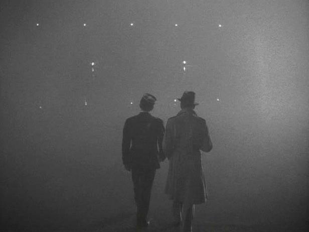 Zwei Männer in Mänteln blicken in einen nebligen Himmel mit Lichtern.
