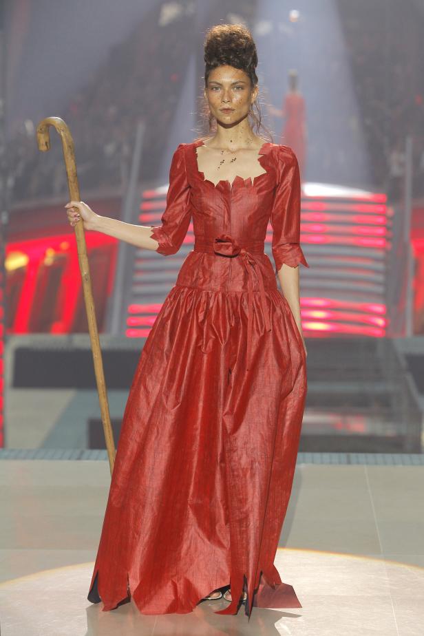 Eine Frau in einem roten Kleid mit Stecken auf einem Laufsteg.