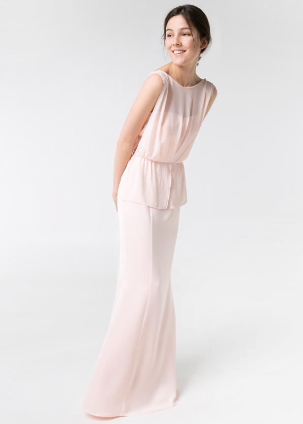 Eine junge Frau in einem hellrosa, ärmellosen Abendkleid lächelt.