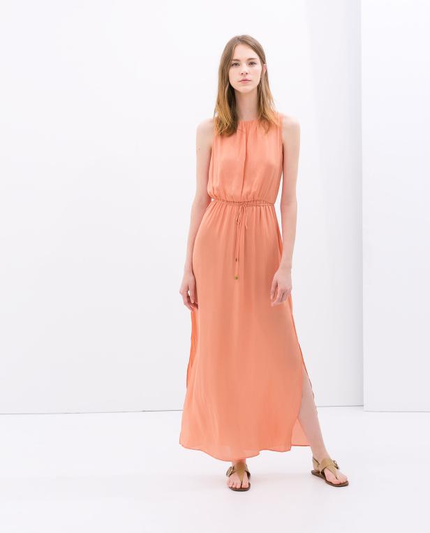 Eine Frau trägt ein lachsfarbenes, ärmelloses Maxikleid mit Sandalen.