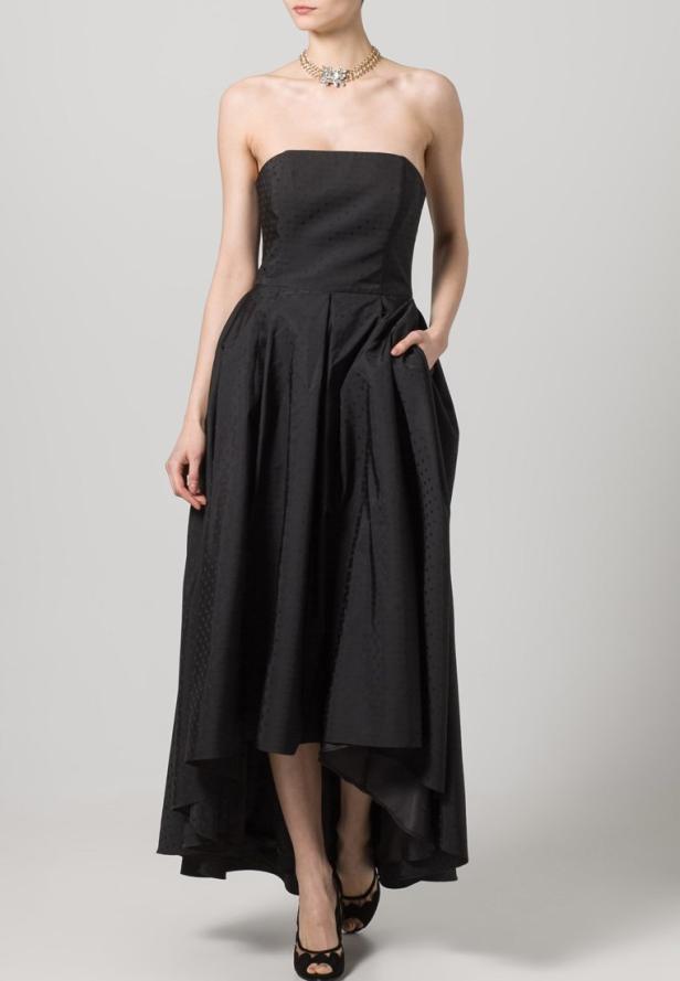 Eine Frau in einem trägerlosen, schwarzen Kleid mit einer Hand in der Tasche.