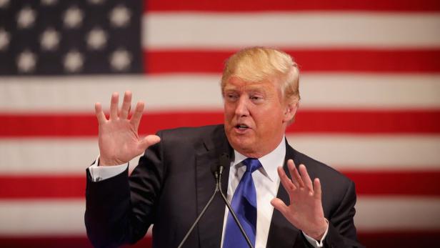Donald Trump gestikuliert vor einer amerikanischen Flagge.