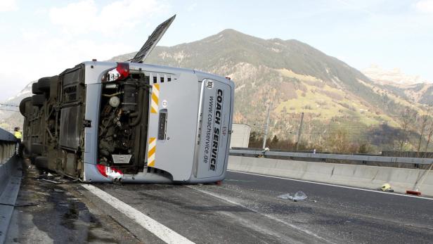 Ein Reisebus liegt auf einer Autobahnseite, im Hintergrund sind Berge zu sehen.