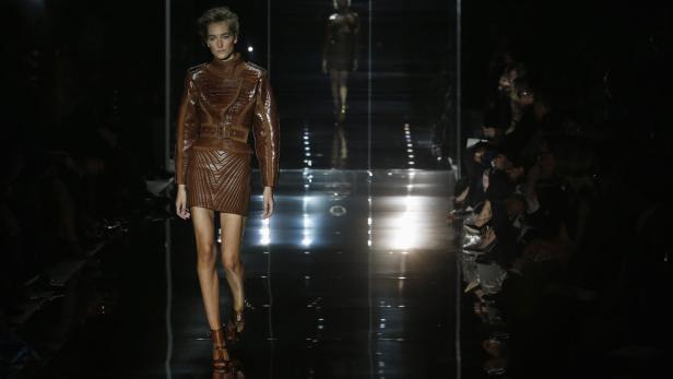 Eine Frau präsentiert ein braunes Lederensemble auf einem dunklen Laufsteg.