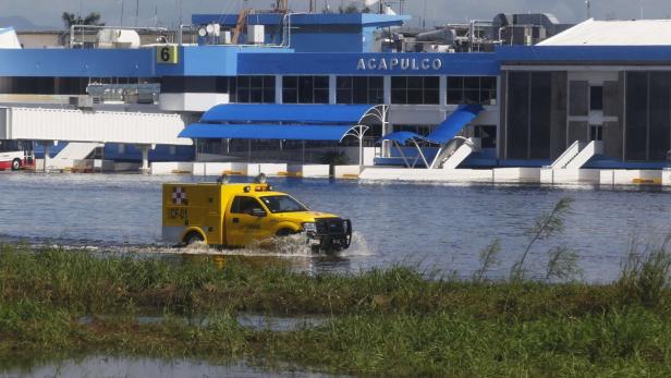 Ein gelbes Fahrzeug fährt durch das Hochwasser vor dem Flughafen Acapulco.