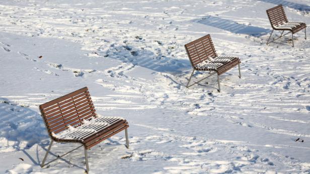 Drei Parkbänke stehen im Schnee.