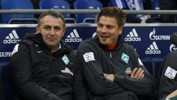 Zwei Männer in Jacken des SV Werder Bremen sitzen auf einer Bank.