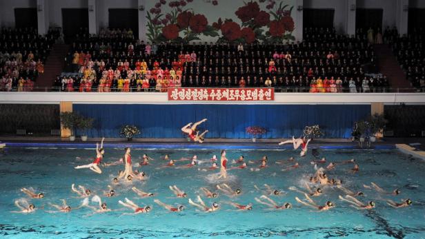 Eine Gruppe Synchronschwimmerinnen bei einer Aufführung in einem Schwimmbad vor Publikum.