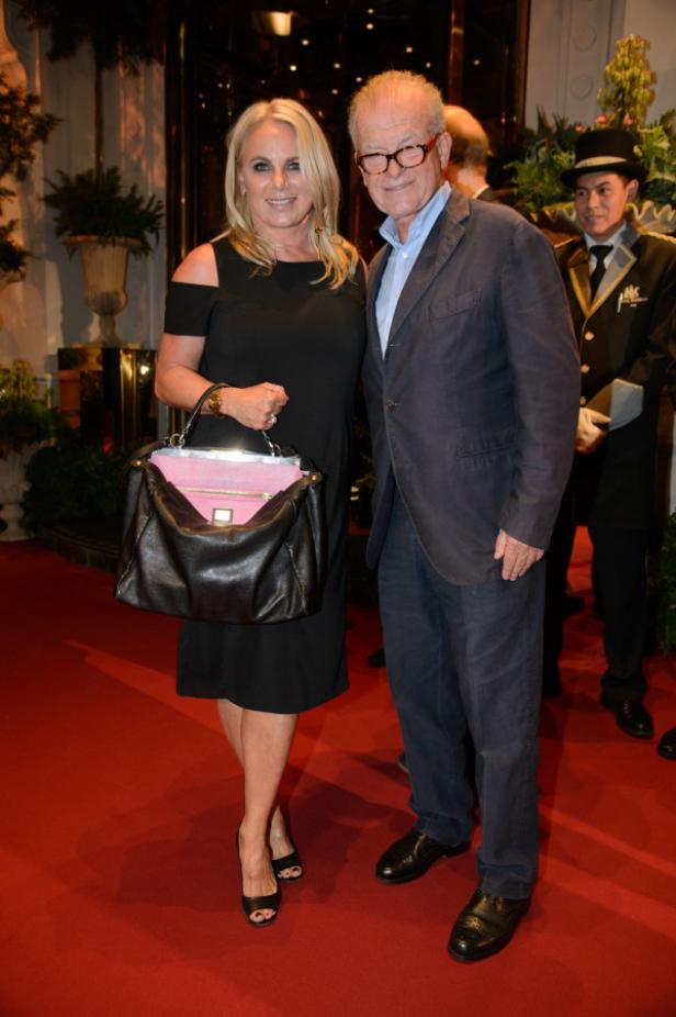 Eine Frau in einem schwarzen Kleid und ein Mann mit Brille posieren auf einem roten Teppich.