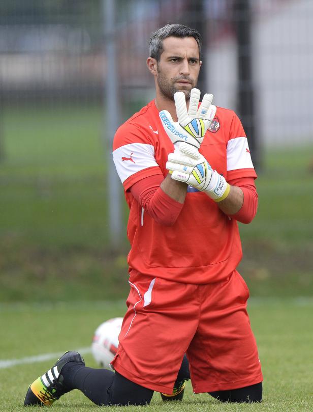 Ein Torwart kniet auf dem Rasen und justiert seine Handschuhe.