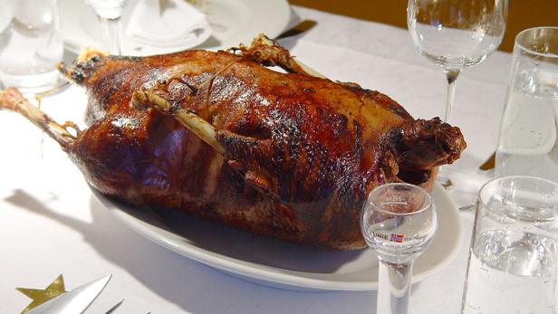 Ein gebratener Truthahn liegt auf einer weißen Platte, umgeben von Gläsern auf einem Tisch.