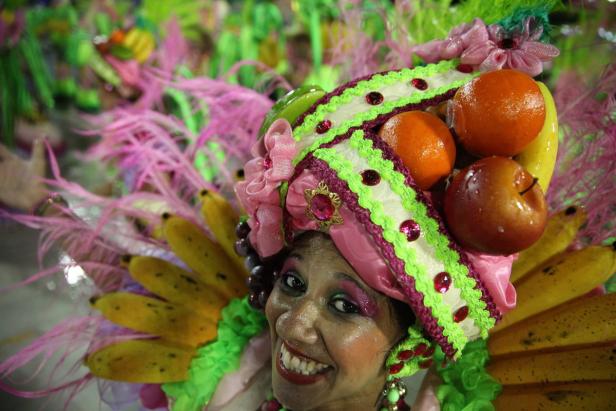 Eine lächelnde Frau mit einem farbenfrohen Kopfschmuck aus Obst und Federn.