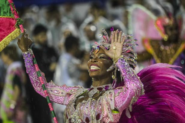 Eine Frau in einem pinkfarbenen, mit Strass besetzten Karnevalskostüm lächelt und winkt.