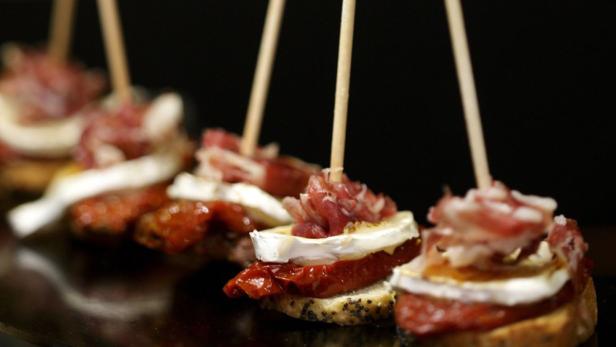 Mehrere Tapas mit Tomaten, Käse und Schinken sind auf Spieße gesteckt.