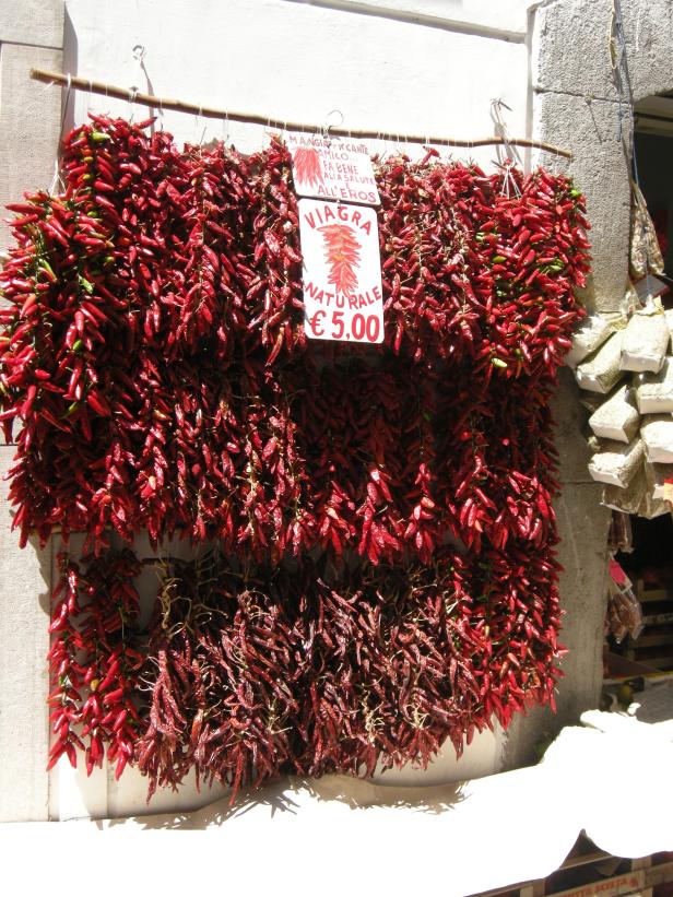 Bündel roter Chilischoten hängen an einer Wand zum Verkauf, beworben als „natürliches Viagra“.
