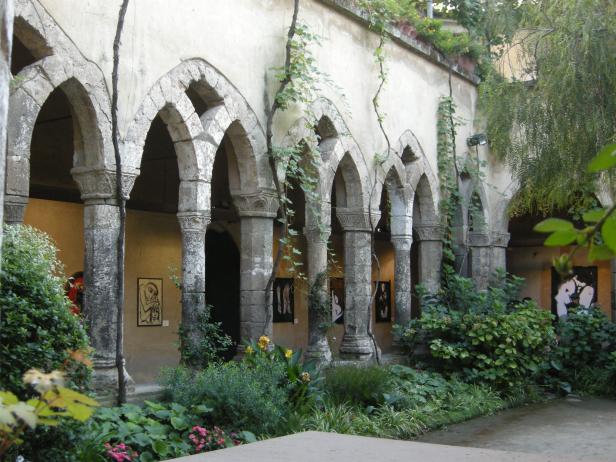 Ein Innenhof mit Steinbögen, Pflanzen und Kunstwerken an den Wänden.