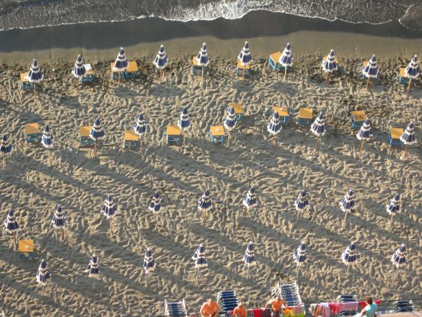 Luftaufnahme eines Strandes mit Sonnenschirmen und Liegestühlen.