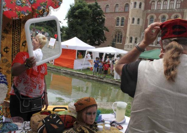 Auf einem Markt hält eine Frau einen Spiegel, der eine weitere Person reflektiert.