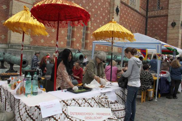 Ein Marktstand der Österreichisch-Indonesischen Gesellschaft mit Speisen und Getränken unter bunten Sonnenschirmen.