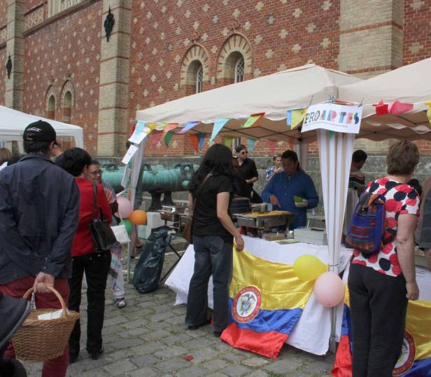 Ein Marktstand mit kolumbianischer Flagge und Imbissangebot vor einem Backsteingebäude.
