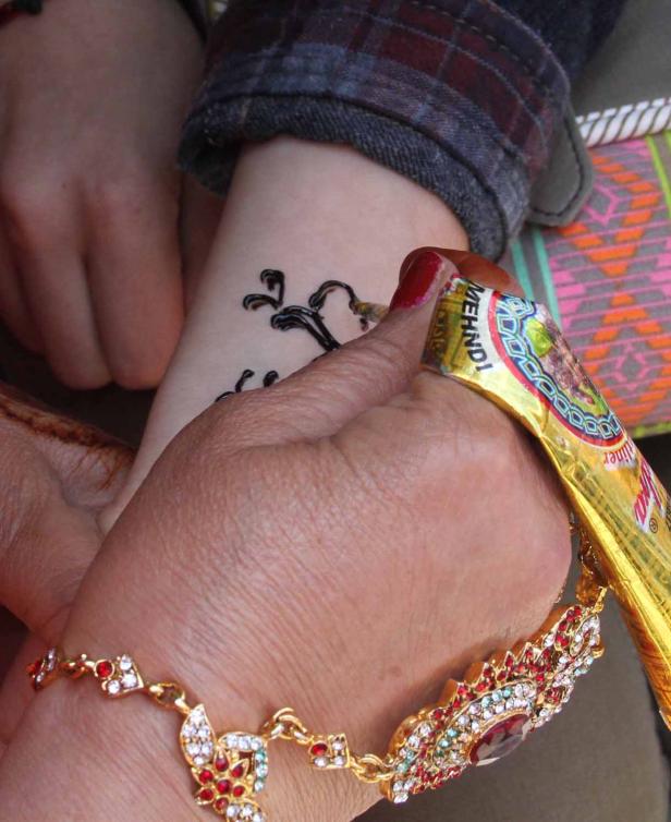 Eine Frau trägt mit einem goldenen Henna-Stift ein Tattoo auf den Arm einer anderen Person auf.