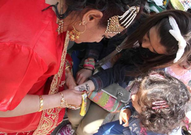 Eine Frau im roten Kleid bekommt ein Henna-Tattoo auf ihre Hand gemalt.