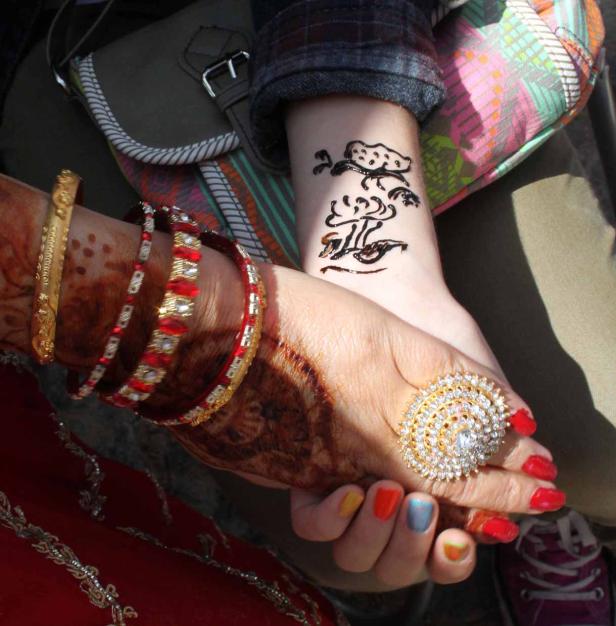 Zwei Frauen halten Hände, geschmückt mit Henna, Armreifen und einem großen Ring.