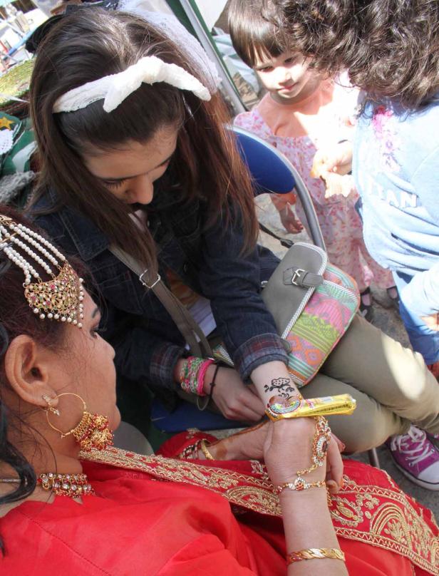 Eine Frau im Sari bekommt ein Henna-Tattoo auf ihren Handrücken gezeichnet.